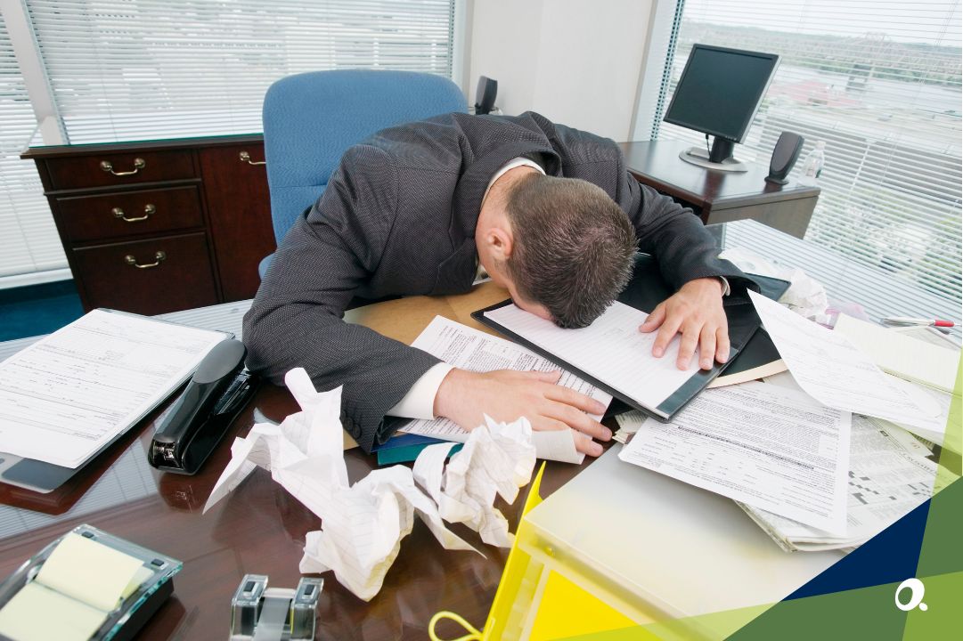 Stressed finance professional in a suit slumped over a cluttered office desk filled with paperwork and crumpled notes, symbolising burnout and overwhelm. Accord Consulting logo in bottom right corner.