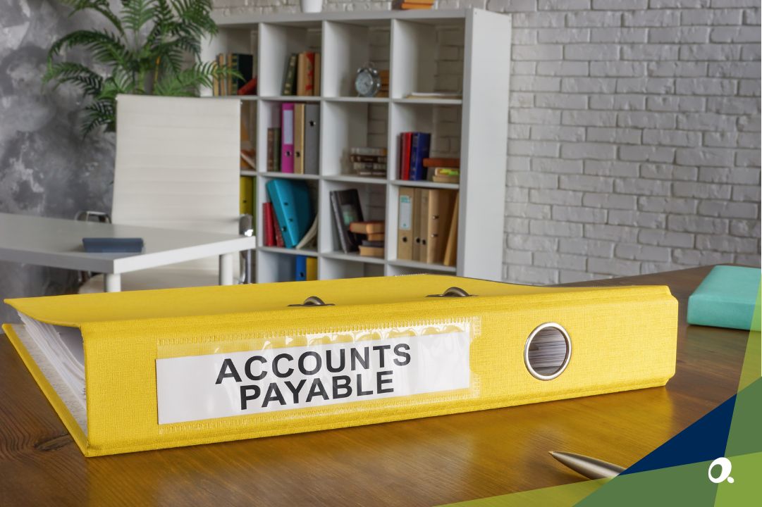 Yellow Accounts Payable binder on an office desk with shelves of files in the background