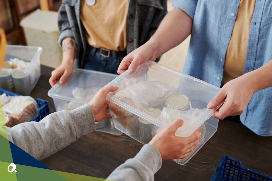 Two people exchanging a clear plastic box filled with canned food and bread