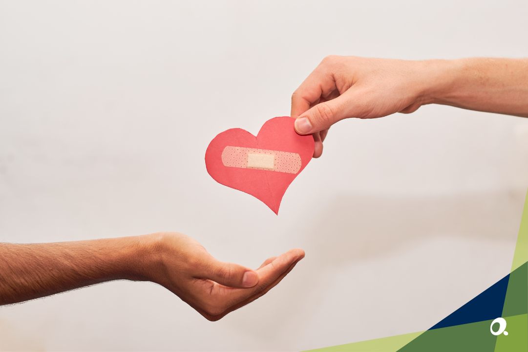 Hand passing a paper heart with a sticking plaster on it to another hand