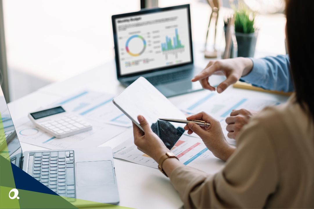 Two people reviewing financial charts and data on a tablet and laptop