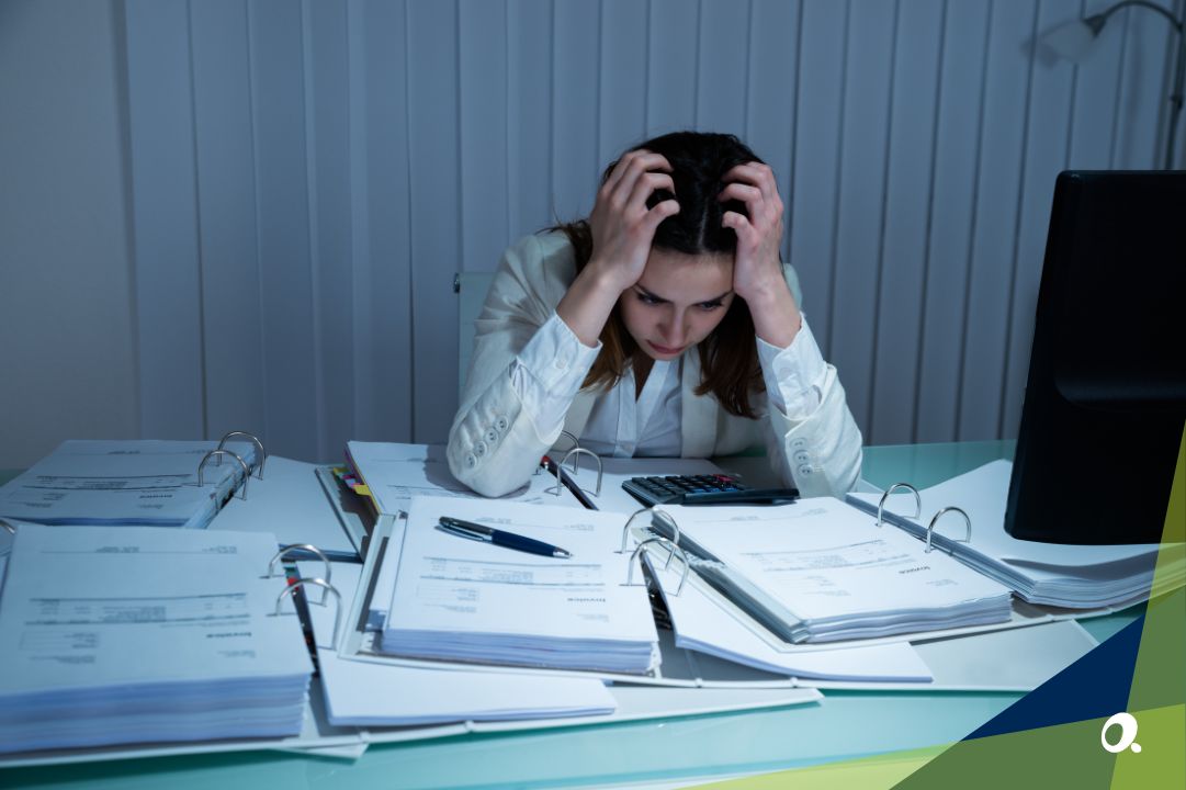 Finance professional under pressure surrounded by paperwork, symbolising compliance and workload challenges on unsupported Sage 1000 software.