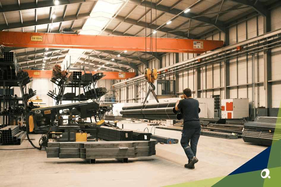 Worker in a warehouse moving large steel pipes with an overhead crane inside an equipment manufacturing facility.
