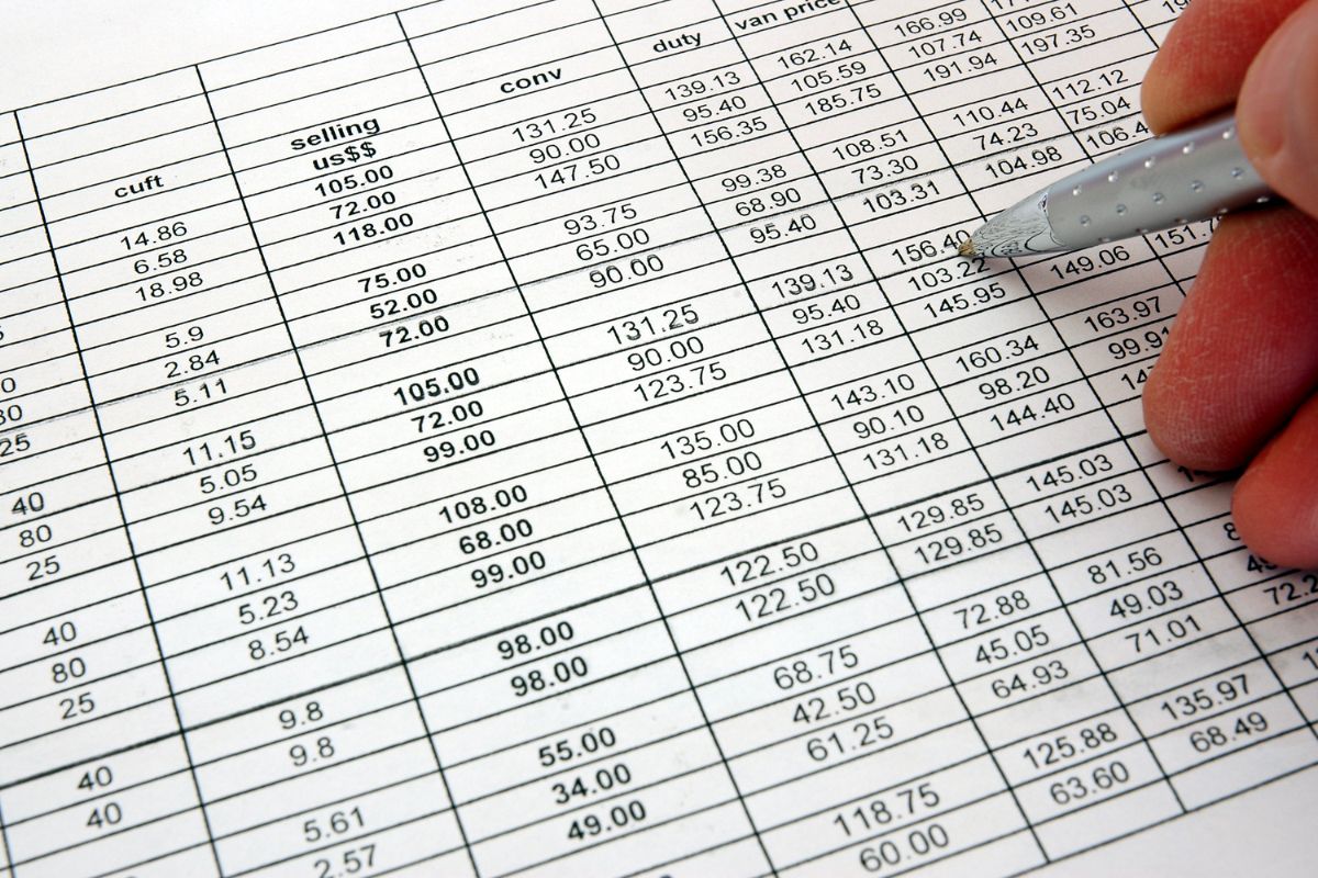 A hand holding a pen over a physical financial spreadsheet